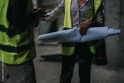 Photos Two architects and engineers in high-visibility vests confer over building plans at a construction site