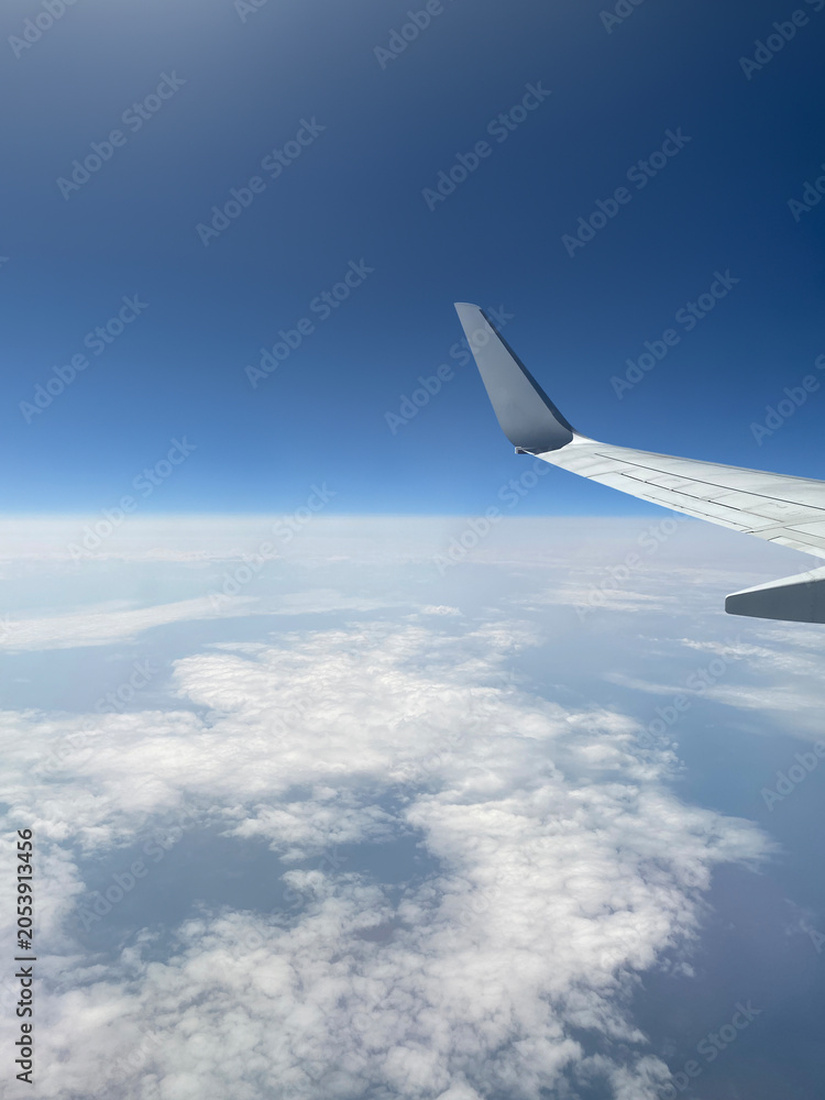 Obraz premium Aerial view of the earth from an aircraft wing above the clouds with a clear blue sky horizon. Flying airplane travel perspective, stratosphere flight altitude, high altitude passenger journey concept