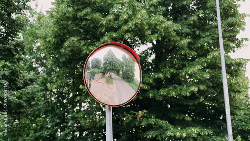 Convex traffic safety mirror on a metal pole reflecting a rural road surrounded by green trees