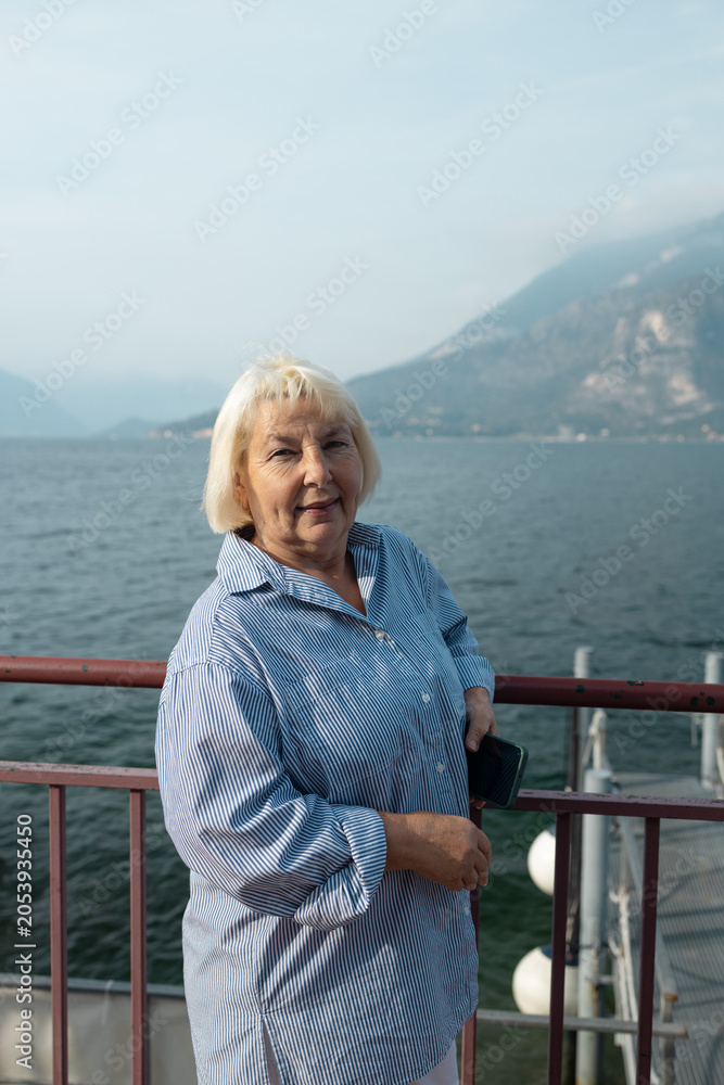 Fototapeta premium Portrait of a happy senior lady with grey hair showing beautiful landscape background on a sunny day during her retirement journey.