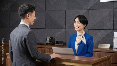 Asian businessman smiling at friendly Asian receptionist during professional interaction at the front desk