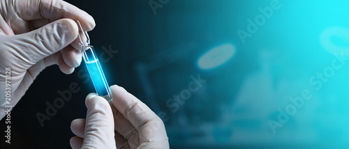 Person in medical gloves holding a glass ampoule with glowing blue liquid in a laboratory.