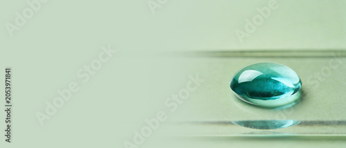 Close-up shot of a rounded teal liquid drop on a glass slide over a light green background.