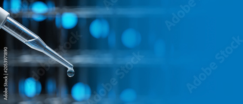 Plastic pipette with a clear liquid droplet against a blurred blue background of laboratory equipment.