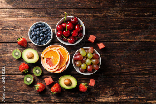 Assorted Fresh Fruits Including Blueberries, Cherries, Citrus Slices, Grapes, Avocado, Kiwi, Strawberries, and Watermelon Cubes on Wooden Background