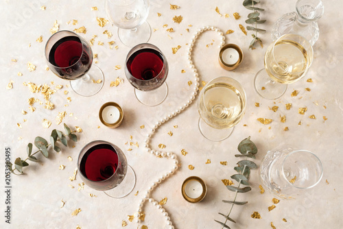 Elegant table setup with red and white wine glasses, candles, eucalyptus, pearl necklace, and gold foil decorations