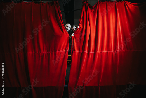 Bild auf Leinwand Two young actors peek from behind a red theater curtain