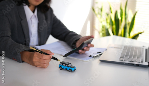 Konstfotografi Businesswoman holding calculator and pointing at miniature car with pen, Calculating car maintenance, tax and insurance costs