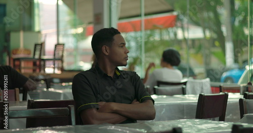 Foto Restaurant worker sitting with arms crossed, staring out window with pensive exp