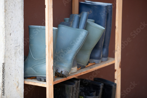 Ensemble de bottes de pluie de différentes taille et de différente couleurs, rangées à l'abri sur une étagère en bois.