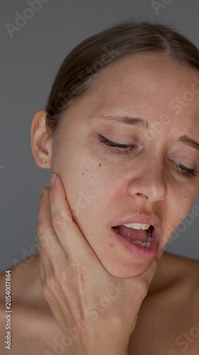 Young woman holding her jaw and moving it with painful expression. Jaw pain, facial tension, TMJ disorder, toothache, muscle spasm and discomfort concept