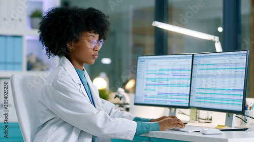 Female scientist analyzing data on dual monitors in modern laboratory, using digital research systems and healthcare informatics for scientific investigation, diagnostics and innovation