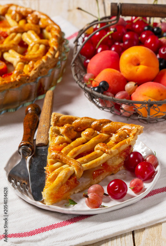 Apricot pie decorated with dough ornament and a metal basket with fruits and berries.
