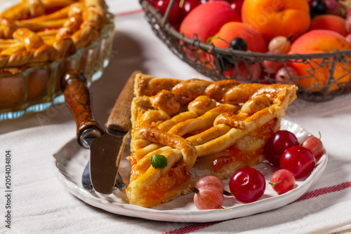 Apricot pie decorated with dough ornament and a metal basket with fruits and berries.