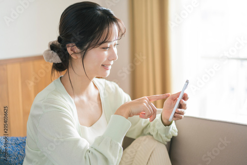 Foto 部屋のソファで笑顔でスマートフォンを操作する若い日本人女性