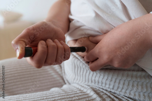 Hands of woman taking insulin on belly at home