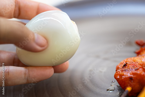 Fotografi Hand holding a freshly peeled hard-boiled egg over a plate.