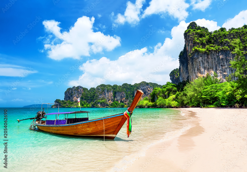 Obraz premium Traditional longtail boat resting on the white sand of Railay Beach near Ao Nang, Thailand. Tropical scenery with turquoise water and dramatic limestone cliffs.