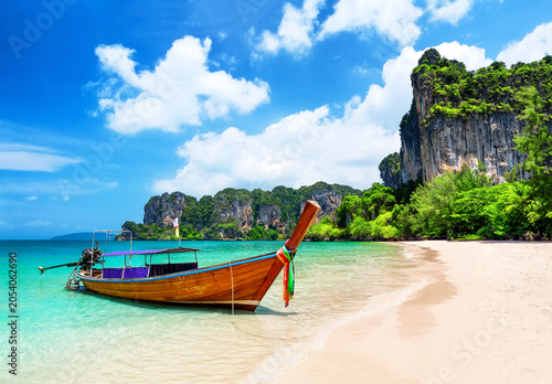 Traditional longtail boat resting on the white sand of Railay Beach near Ao Nang, Thailand. Tropical scenery with turquoise water and dramatic limestone cliffs.