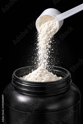 White powder pours from scoop into black container. Powder falls in slow motion against dark background. Clean, minimalist shot highlights texture and flow. Ideal for fitness, nutrition