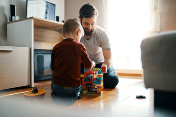 Father and son sitting on the floor at home playing together with building bricks