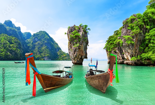 Iconic view of James Bond island with thai traditional wooden longtail boat and beautiful turquoise water in Phang Nga bay, Thailand.