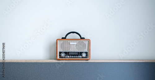 Photos Vintage Portable Radio on a Wooden Shelf,A retro-style portable radio with a wooden frame and handle sitting on a modern wooden shelf against a plain white wall