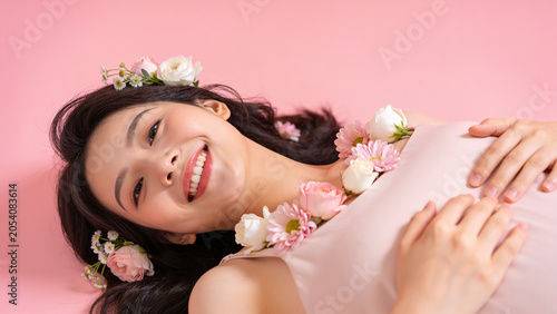 Smiling woman lying on pink background with flowers on her hair. concept of happiness