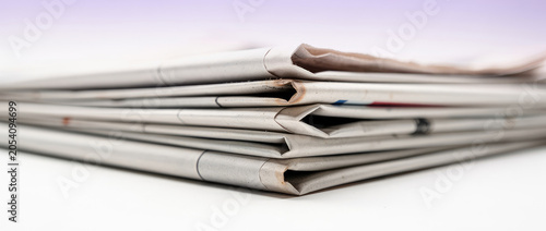 A stack of newspapers lies on a white surface with a soft purple background.