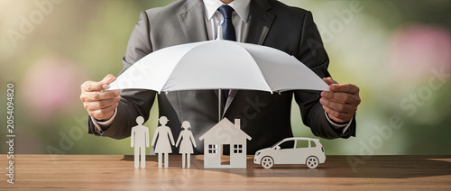 Insurance agent protecting family, house, and car with umbrella.