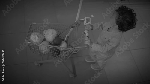 Top-down view of child pushing small shopping cart across tiled supermarket floor