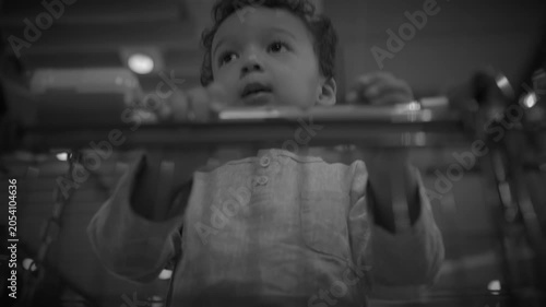 Low-angle black-and-white toddler standing behind a shopping cart handle in a store