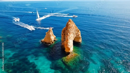 Aerial view of large rock formations in the blue ocean with small speed boats cruising nearby