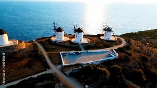 Aerial view of traditional white windmills on a hill overlooking the blue sea at sunset