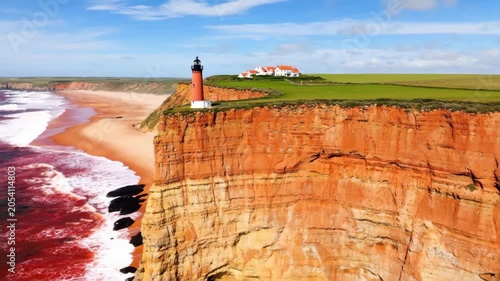 Tall lighthouse standing on a high orange cliff edge above the blue ocean beach