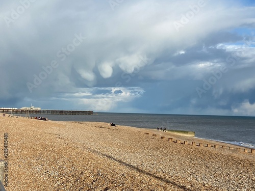 Rare mammatus cloud formation hanging over the sea before a thunderstorm. Dramatic storm clouds with unusual pouch-shaped formations above a beach, creating an atmospheric weather background with copy