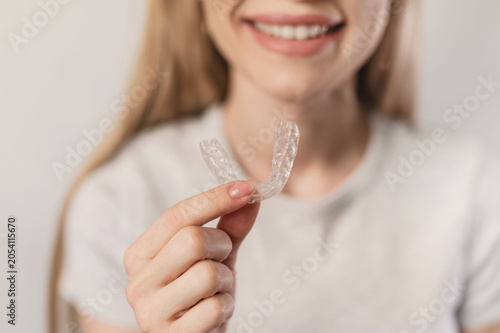Closeup smiling girl holds transparent silicone night guard to protect teeth from wear. Bruxism. Orthodontic treatment of malocclusion, teeth straightening with aligners.