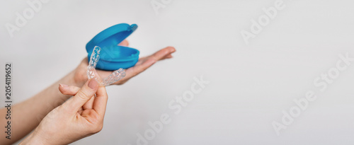 A soft silicone mouth guard and container in a woman's hands on a white background. Bruxism as a stress response. banner copy space