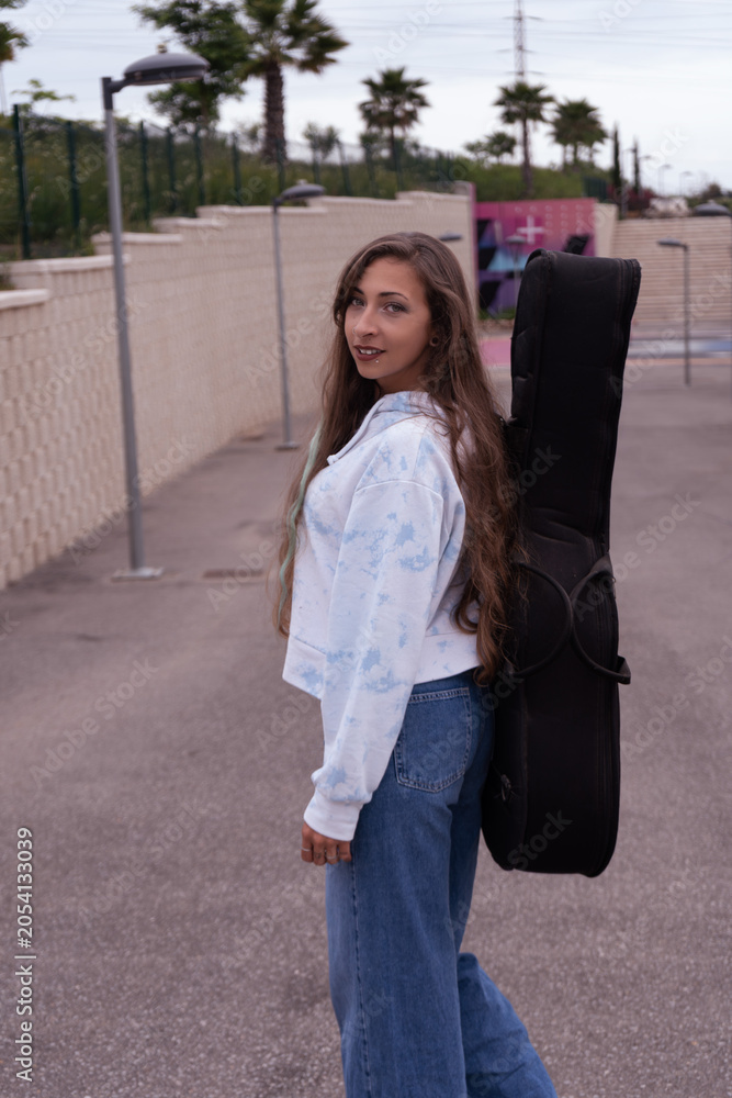 Fototapeta premium Young woman carrying guitar case walking urban park path