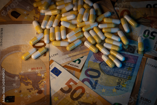 Photographie de nombreuses gélules disposées sur des billets en euros. Cette image symbolise les dépenses de santé, l’industrie pharmaceutique, le remboursement des soins