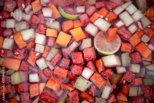 Close up of a refreshing drink with a mix of clear ice cubes and fresh fruit slices, emphasizing vibrant fruit colors