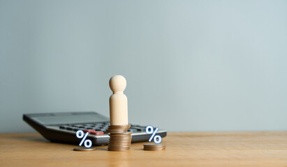 Financial concept with wooden figure on coin stacks, percentage signs and calculator on table