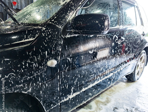 Foto Water and soap mix create bubbles on black car during cleaning session at local