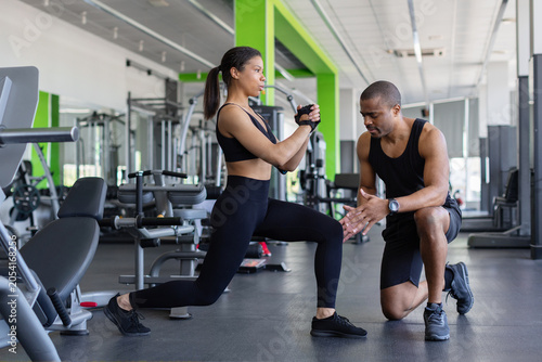 Fotografie Personal trainer supervising a young woman during a lunge exercise in fitness ce