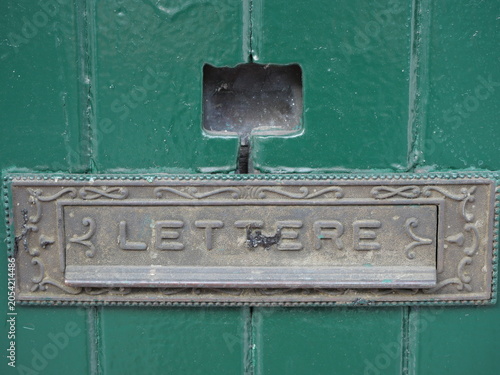 This vintage-style, antique brass letter slot is mounted on a textured, dark green wooden door.