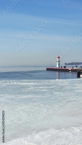 Lighthouse on a pier in winter with frozen water and ice in the foreground