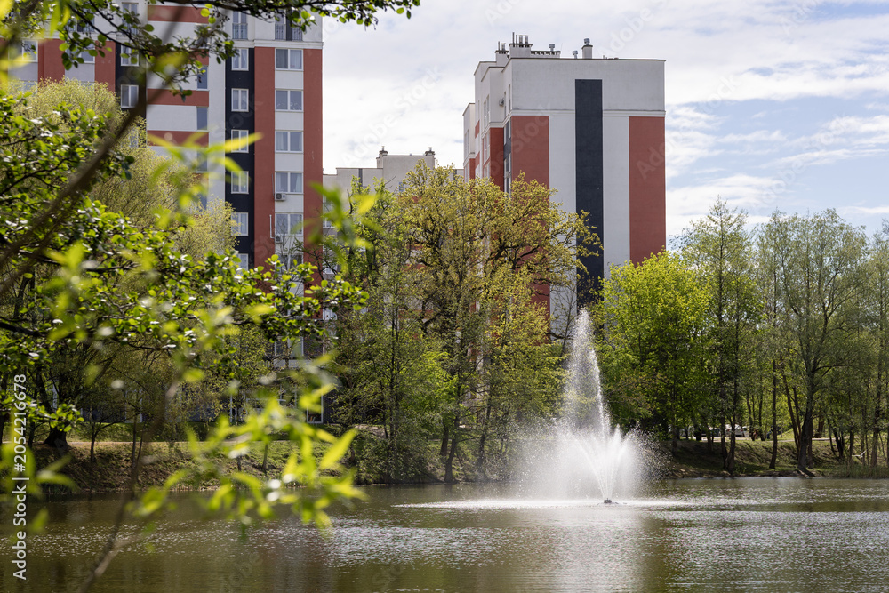 Fototapeta premium Residential buildings by lake with fountain in daytime
