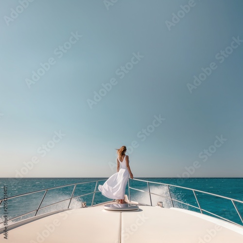 Young woman in white dress standing on yacht bow over turquoise sea