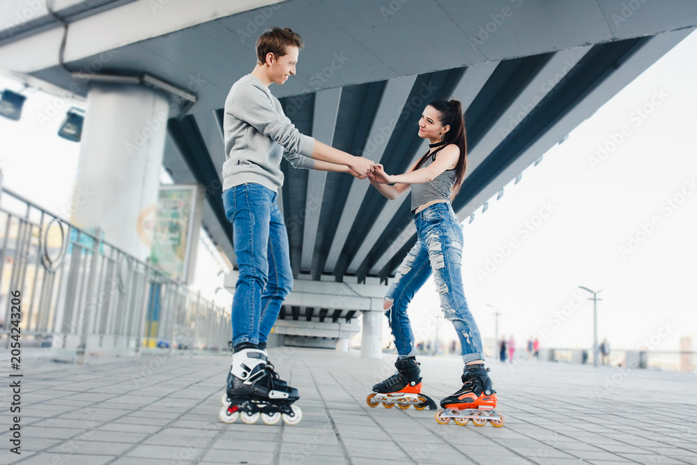 Fototapeta premium Young couple rollerblading together holding hands