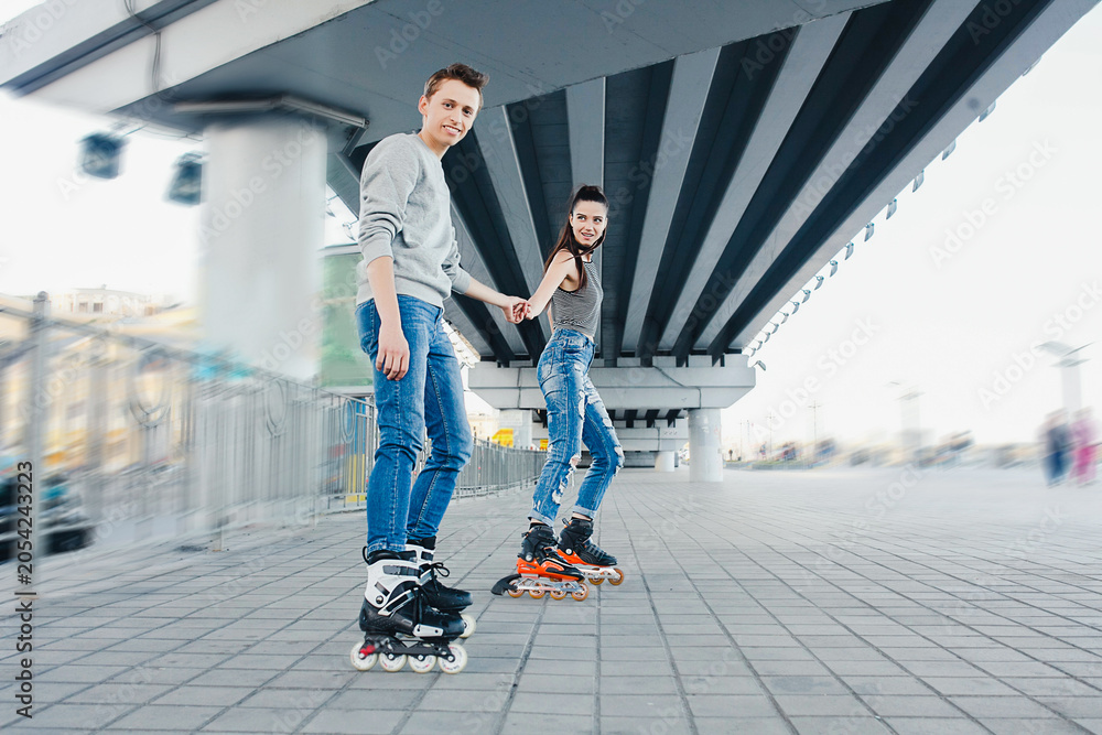 Obraz premium Young couple rollerblading holding hands under bridge